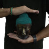 A large brass buddha head sculpture with a textured teal topknot held gently in hands