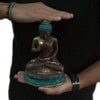 A large brass seated buddha statue with turquoise and gold accents meditating on a lotus base