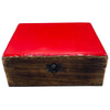 A large ceramic glazed wooden box with a glossy red lid and black metal clasp on a rustic wooden surface