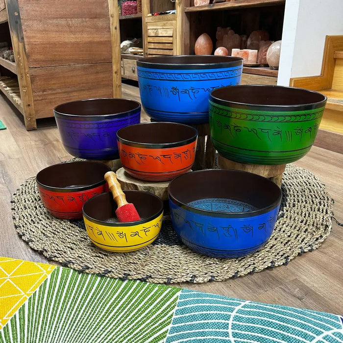 Set of seven singing bowls in large chakra colors with engraved sanskrit mantras including a blue bowl and black rims