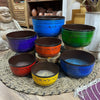 Set of seven singing bowls in vibrant colors with engraved sanskrit and decorative borders including a blue bowl large chakra