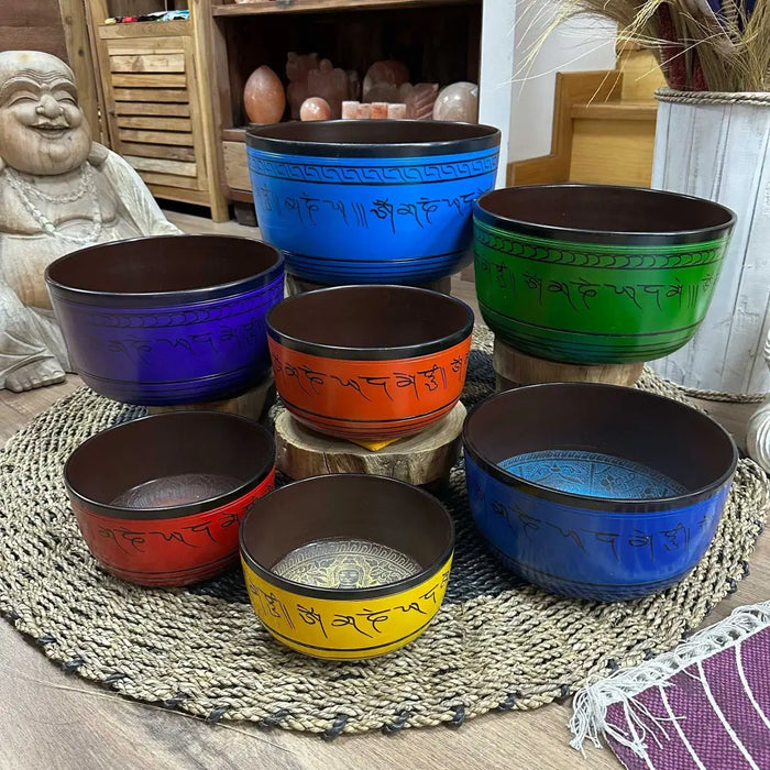 Set of seven singing bowls in vibrant colors with engraved sanskrit and decorative borders including a blue bowl large chakra