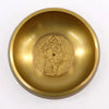 Large golden brass singing bowl with embossed ganesh deity at center for meditation and sound healing