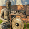 Bronze buddha statue with detailed head seated in meditation beside a black patterned large gong on wooden stand 80cm