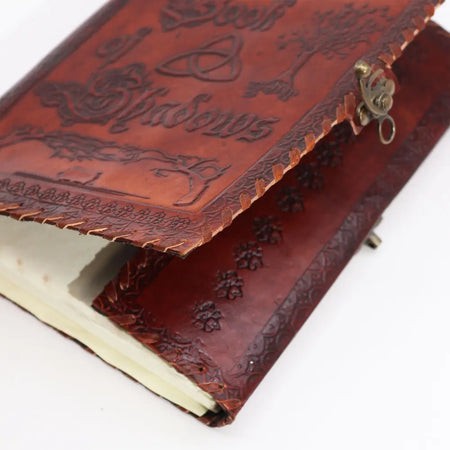 A large dark tan leather notebook with embossed designs and a brass clasp for use as a book of shadows