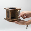 A rustic square mango wood oil burner with carved lattice panels and two black ceramic bowls featuring an elephant design