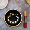 Black singing bowl set with gold rim and moon phase design with wooden mallet to help release negative emotions