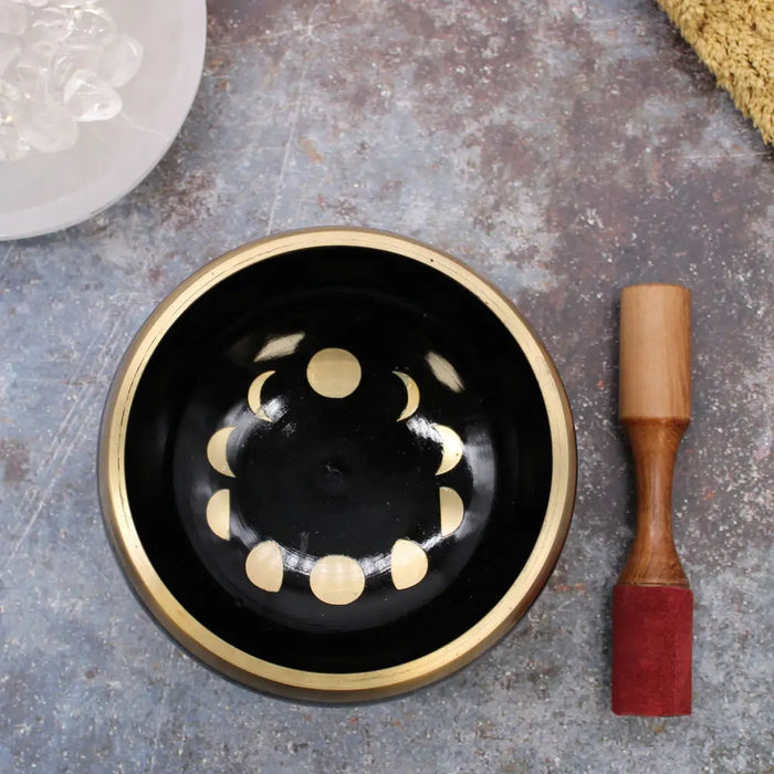 Black singing bowl set with gold rim and moon phase design with wooden mallet to help release negative emotions