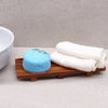 A round blue bath bomb with lavender flakes on a large naseberry wood soap tray with a textured surface