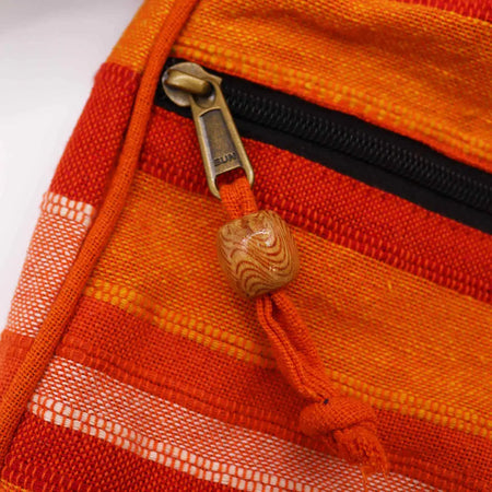 A wooden bead with swirling grain on an orange fabric zipper pull of a large nepal sling bag sunrise orange