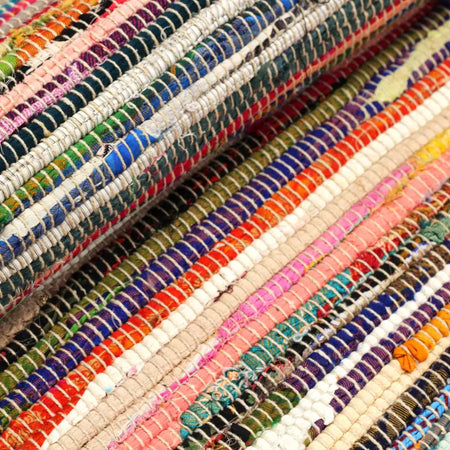A large handwoven rag rug with random colours in a striped pattern made of multicolored yarns with frayed edges