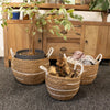 Three woven seagrass cotton baskets with white stripes and rope handles holding blankets and driftwood