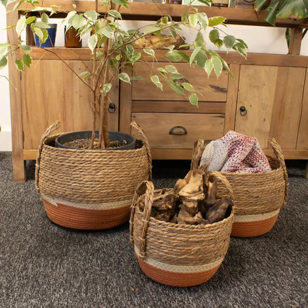 Three woven seagrass and straw baskets with terracotta bases and handles holding different items with varied diameters