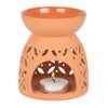 Large terracotta ceramic oil burner with leaf and triangle cutout patterns holding lit tealight candle for home decor