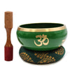 Large green singing bowl set with gold rim and om symbol resting on a patterned cushion from tree of life