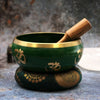 Large green tibetan singing bowl set with gold rim and om symbols resting on a patterned cushion