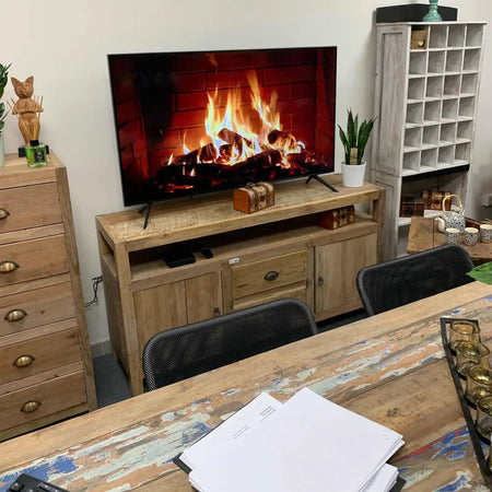 Large tv stand made of recycled wood holding a flat-screen TV showing a fireplace with orange and yellow flames