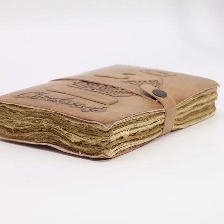 Light tan leather notebook check mate with embossed floral and script detailing and a matching strap closure