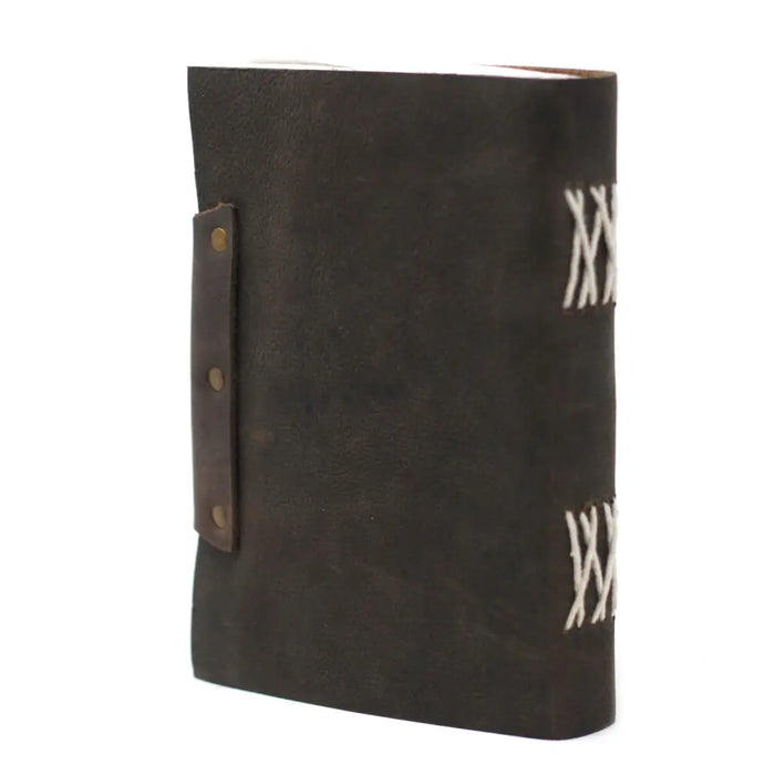 Dark brown leather notebook with white stitching and a leather strap fastened by brass rivets measuring 7 by 5 inches