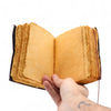 A hand holds an open leather notebook with aged yellow deckled edge pages and dark brown leather binding