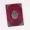 A rich burgundy leather notebook with a silver hamsa hand emblem and intricate metallic corner details, 10 by 7 inches