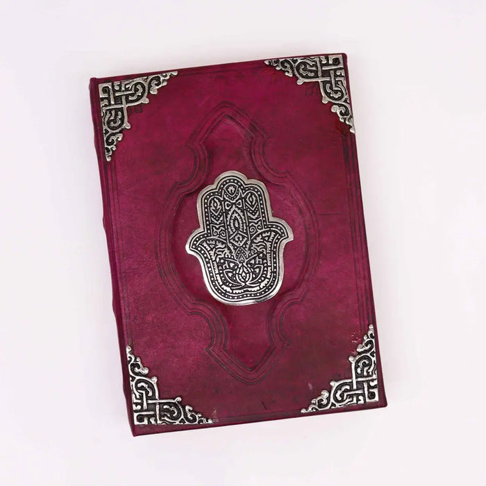 A rich burgundy leather notebook with a silver hamsa hand emblem and intricate metallic corner details, 10 by 7 inches