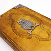 A leather notebook with an aged tan cover featuring a silver owl charm with detailed feathers and beady eyes