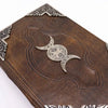 Brown leather notebook with silver triple moon emblem and ornate corner details measuring 10 by 7 inches