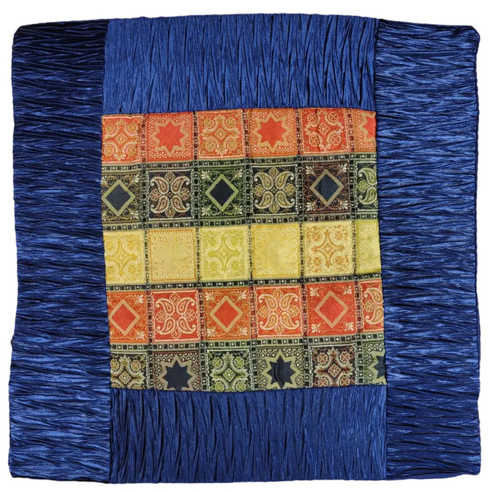 A lightly padded silk-effect cushion cover with a colorful patchwork quilt and blue ruffled border for standard cushions