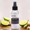 A sleek silver spray bottle of lime and ginger essential oil mist with black nozzle surrounded by lime slices ginger roots and witch hazel