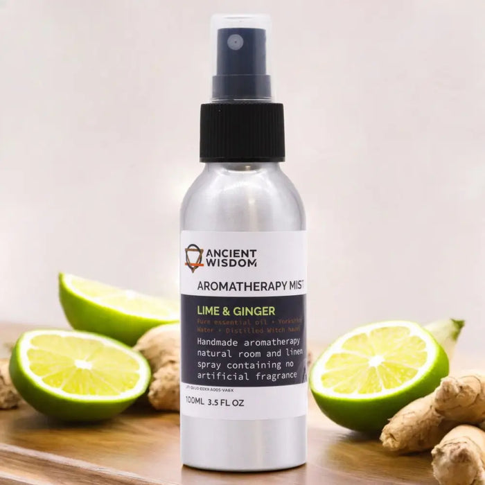A sleek silver spray bottle of lime and ginger essential oil mist with black nozzle surrounded by lime slices ginger roots and witch hazel