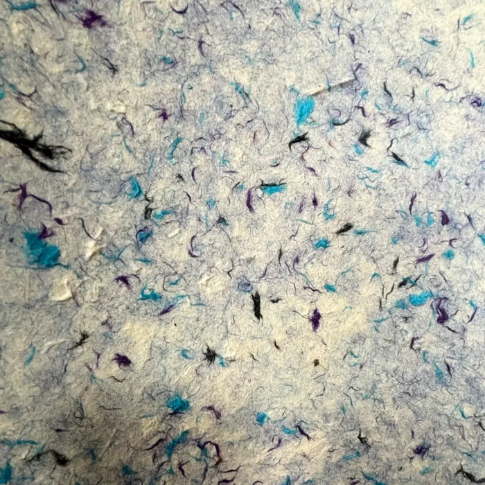 A sheet of off-white lokta paper with scattered blue cotton and purple fibers for gift wrapping use