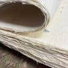 A stack of off-white textured lokta craft paper with visible fibers and lavender flower print for gift wrapping