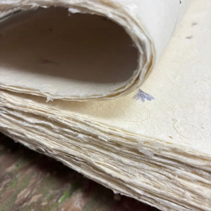 A stack of off-white textured lokta craft paper with visible fibers and lavender flower print for gift wrapping