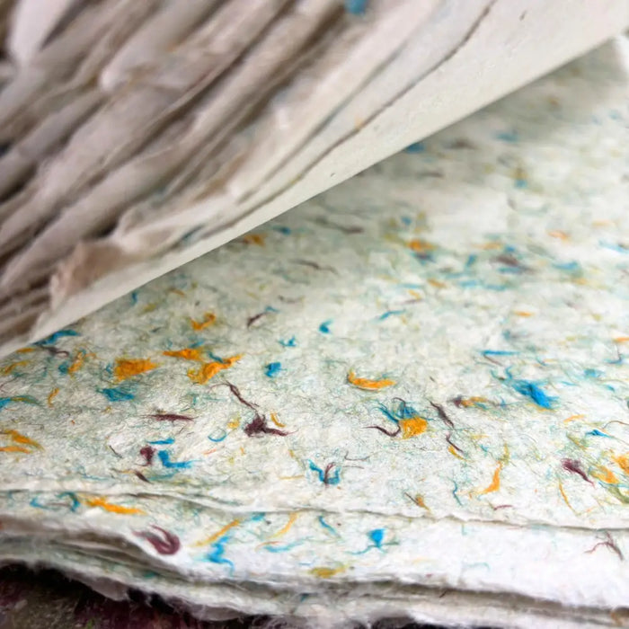Stack of off-white lokta paper with blue orange and brown speckles made from cotton fibres green cotton brand