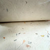 A roll of off-white lokta paper with mixed floral cotton dried leaves in gray brown and yellow embedded in the texture