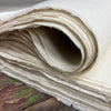 A stack of off-white textured lokta craft handmade paper with visible fibers and uneven edges for gift wrapping