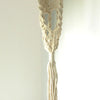 Cream-colored long macrame pot holder with rattan hoop featuring intricate knotting and a tassel at the bottom