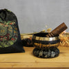 Black tibetan lotus flower singing bowl with gold rim and sanskrit inscriptions resting on ring pillow with wooden mallet