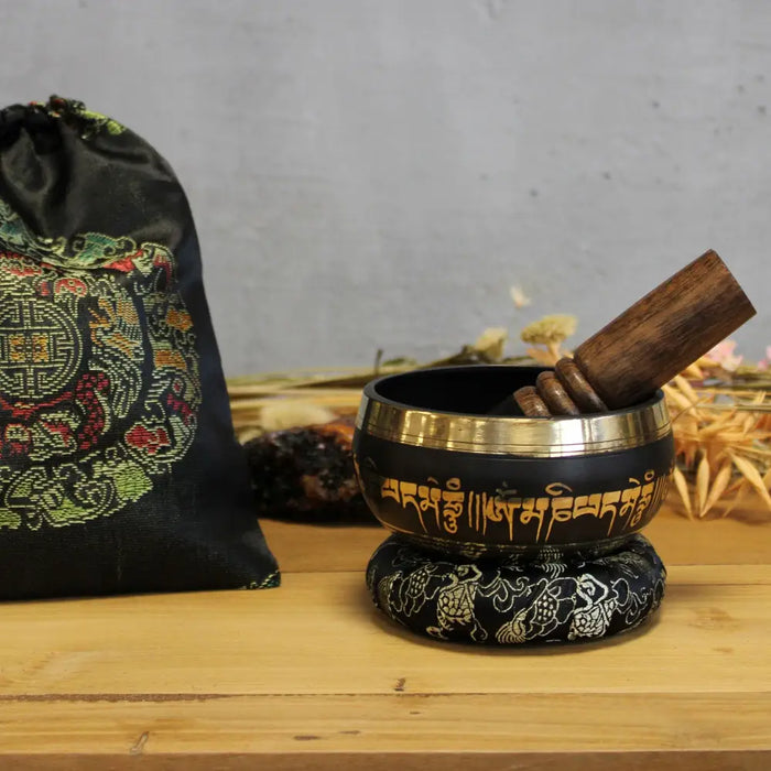 Black tibetan lotus flower singing bowl with gold rim and sanskrit inscriptions resting on ring pillow with wooden mallet
