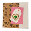 A milford haven love themed greetings card with a white tag, gold lace heart frame, and green glitter heart inside