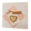 A cream paper love card with a laser-cut wooden heart over pink floral paper and a milford haven brown tag with twine