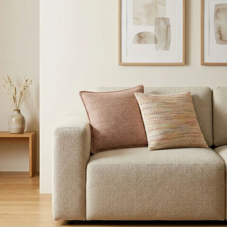 Beige textured fabric sofa with two decorative pillows featuring a burgundy squares cushion cover and multicolored weave