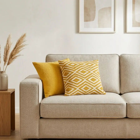 Beige upholstered sofa with two mustard yellow cushion covers one solid and one with a geometric diamond pattern