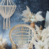 Beige rattan peacock chair with intricate woven backrest and curved seat next to natural cotton rope chandelier