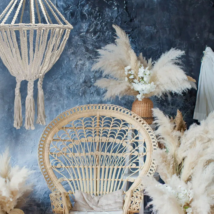 Beige rattan peacock chair with intricate woven backrest and curved seat next to natural cotton rope chandelier