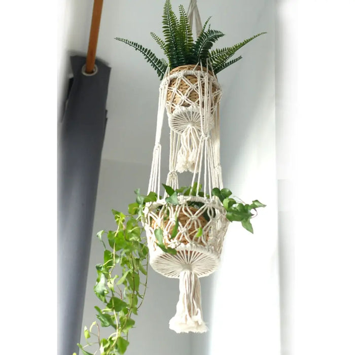 White macrame pot holder double holder with two woven natural fiber baskets holding potted fern and ivy plants