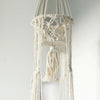 A cream-colored macrame pot holder double holder with intricate knotwork and a fringed tassel made from cotton rope