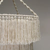 Cream-colored macrame chandelier made of soft cotton rope with intricate woven cords and long fringe hanging decor