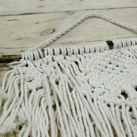 White macrame wall hanging with intricate knotting and long fringe made from cotton for home decor